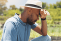 Man sitting in field with hat on and hand rested against his head