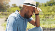 Man sitting in field with hat on and hand rested against his head