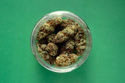 Glass jar filled with dried cannabis buds on a green background