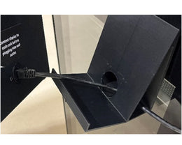 Black electronic device with a cable plugged into it on a light-colored floor.